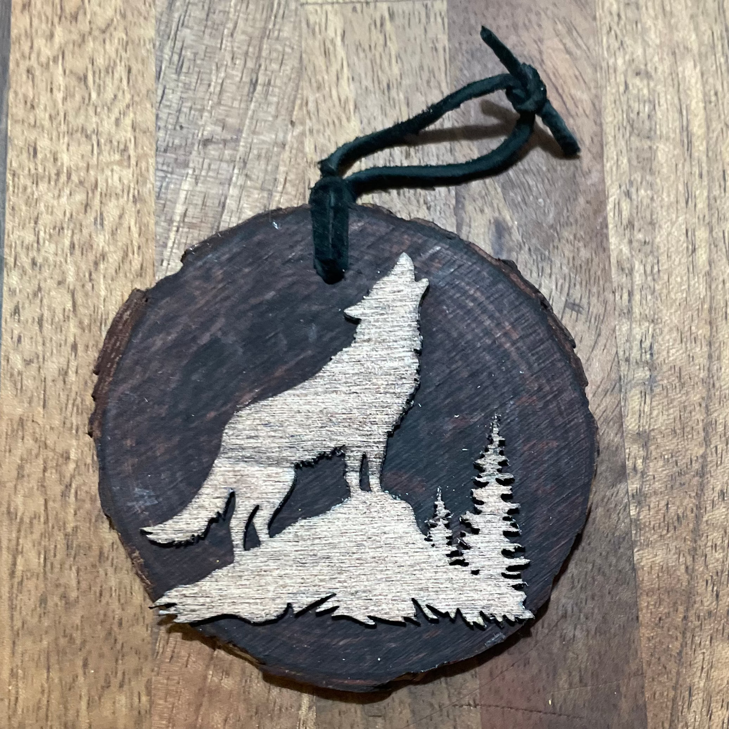 Wooden ornament with a wolf laser-cut design in a light stain on a natural wood round. Tied with a black leather cord.