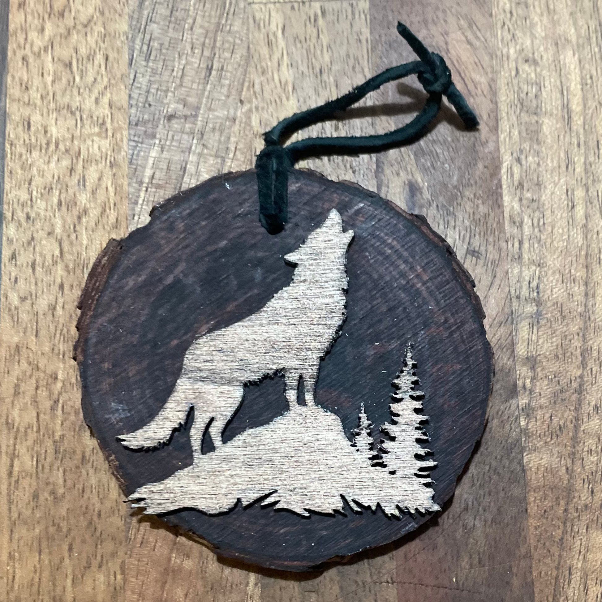 Wooden ornament with a wolf laser-cut design in a light stain on a natural wood round. Tied with a black leather cord.